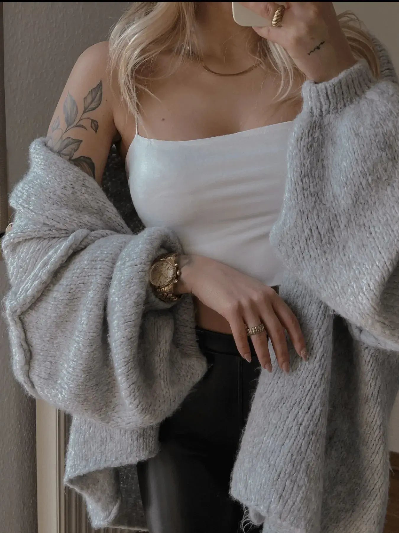 Woman wearing oversized grey cardigan, white cami, and black pants, showcasing modern chic style with luxe comfort and textured fabric.