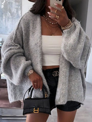 Model wearing oversized open front cardigan with dropped shoulders, paired with a white crop top and black shorts, holding a handbag.