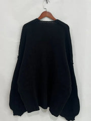 Back view of an oversized black open front dropped shoulder cardigan hanging on a wooden hanger, showcasing its textured fabric.