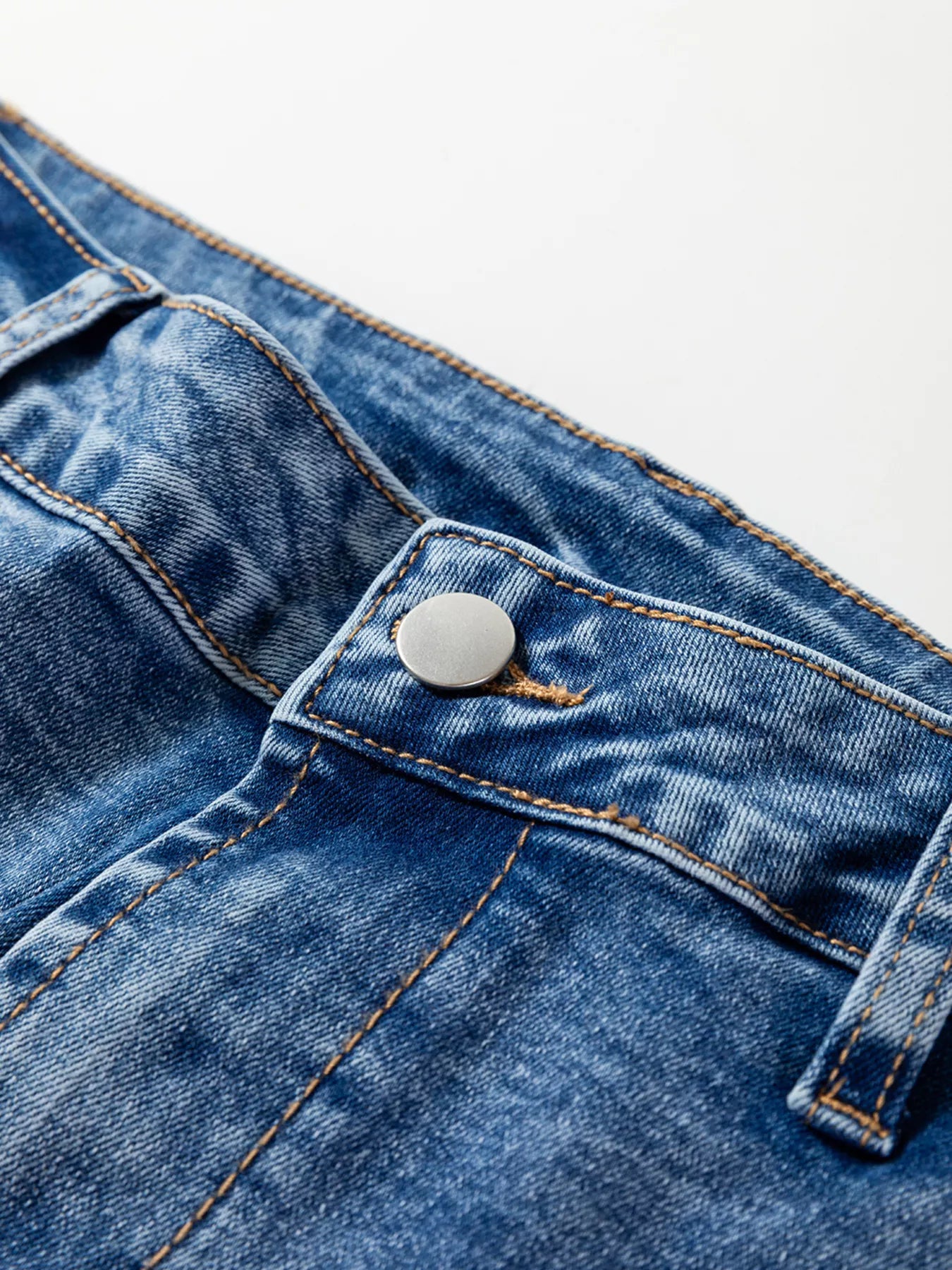 Close-up of seam detail loose fit cropped jeans highlighting button and stitching on denim fabric.