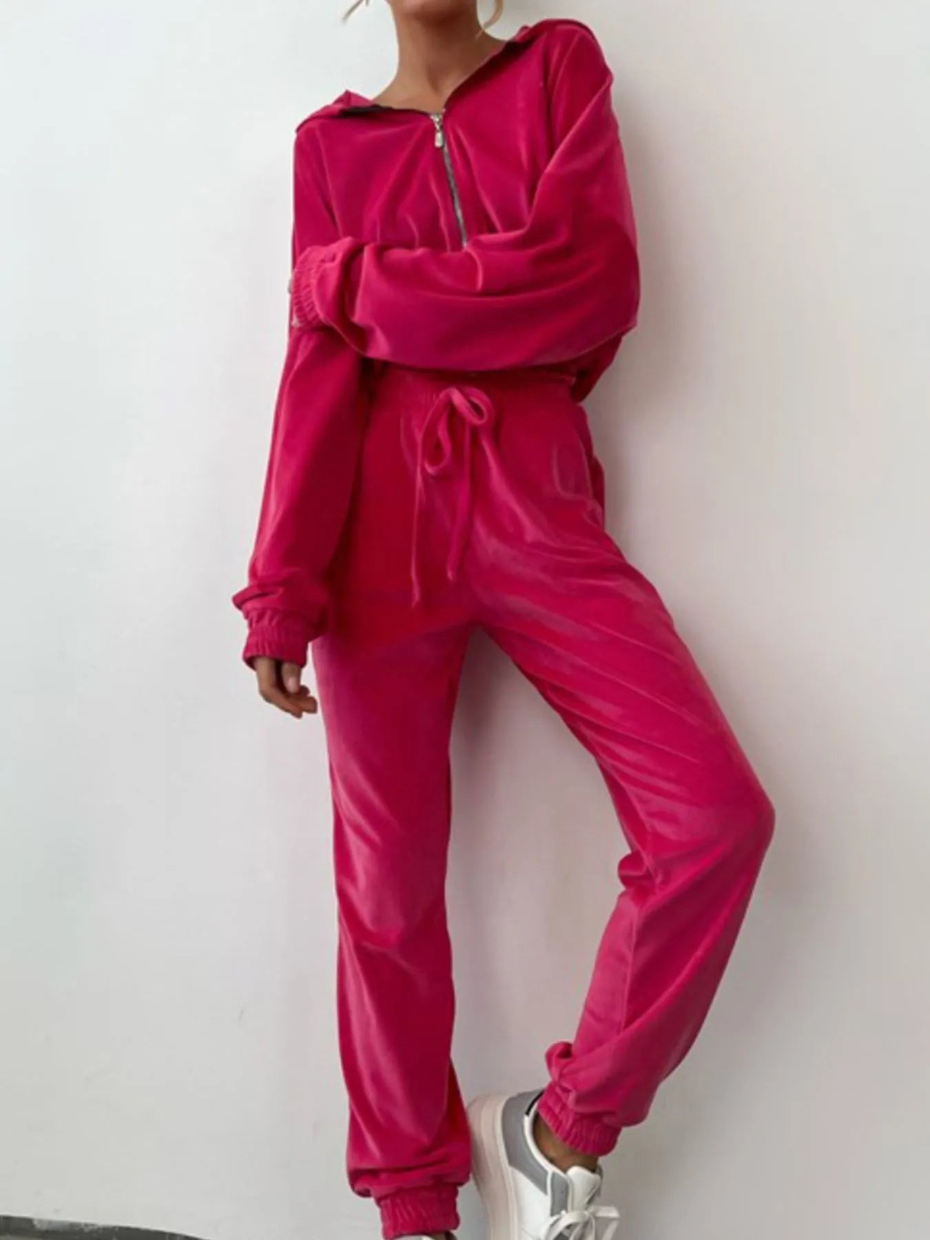 Woman wearing a plush fuchsia velour zip up long sleeve top and pants set, featuring a drawstring waist and side pockets, against a white background.