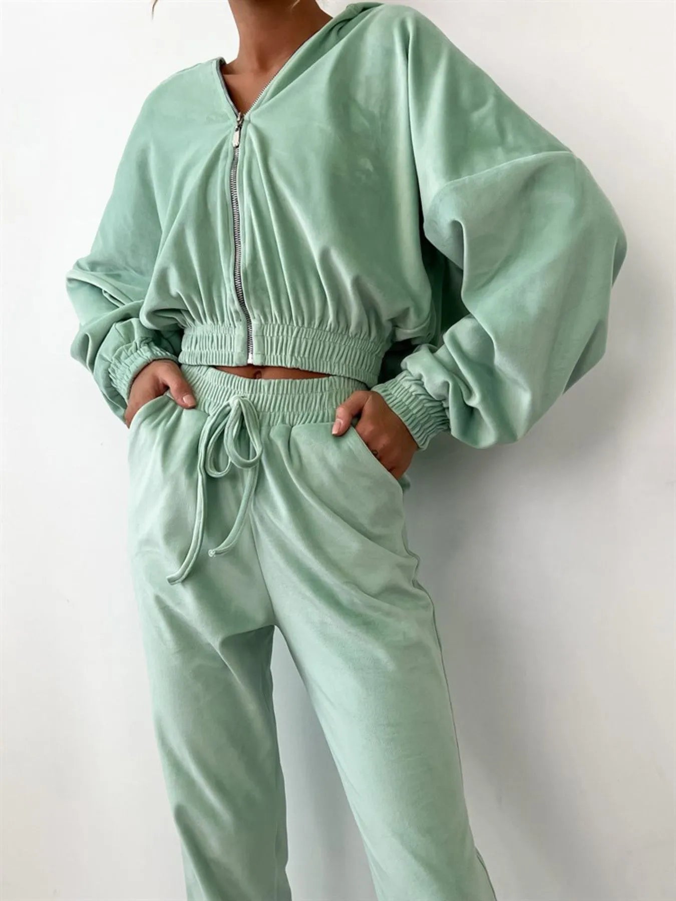 Sky blue zip up long sleeve top and pants set with a drawstring waist on a model, featuring a plush velour fabric for a cozy fit.